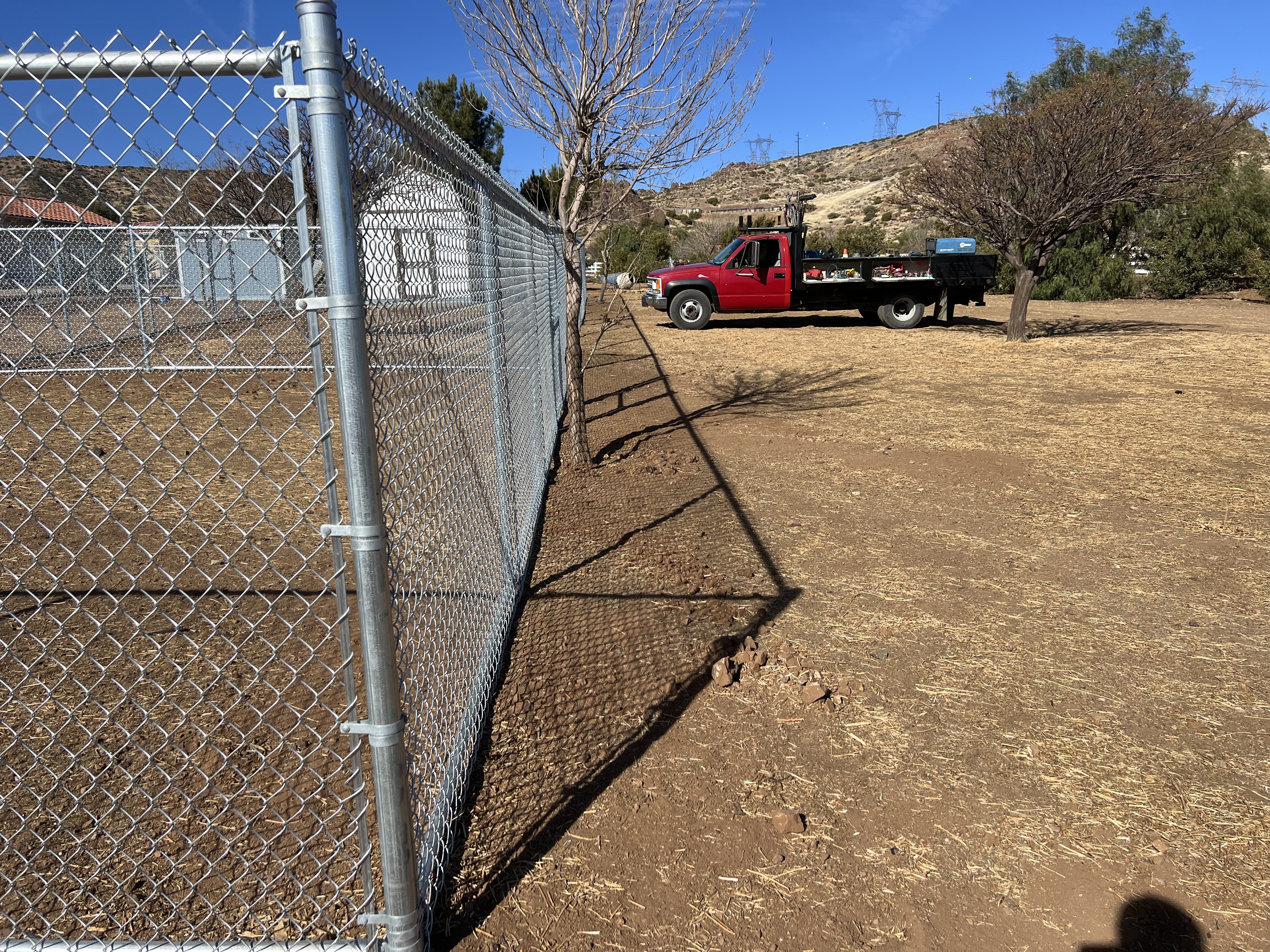 Galvanized chain-link fence run along hillside terrain with work truck in background