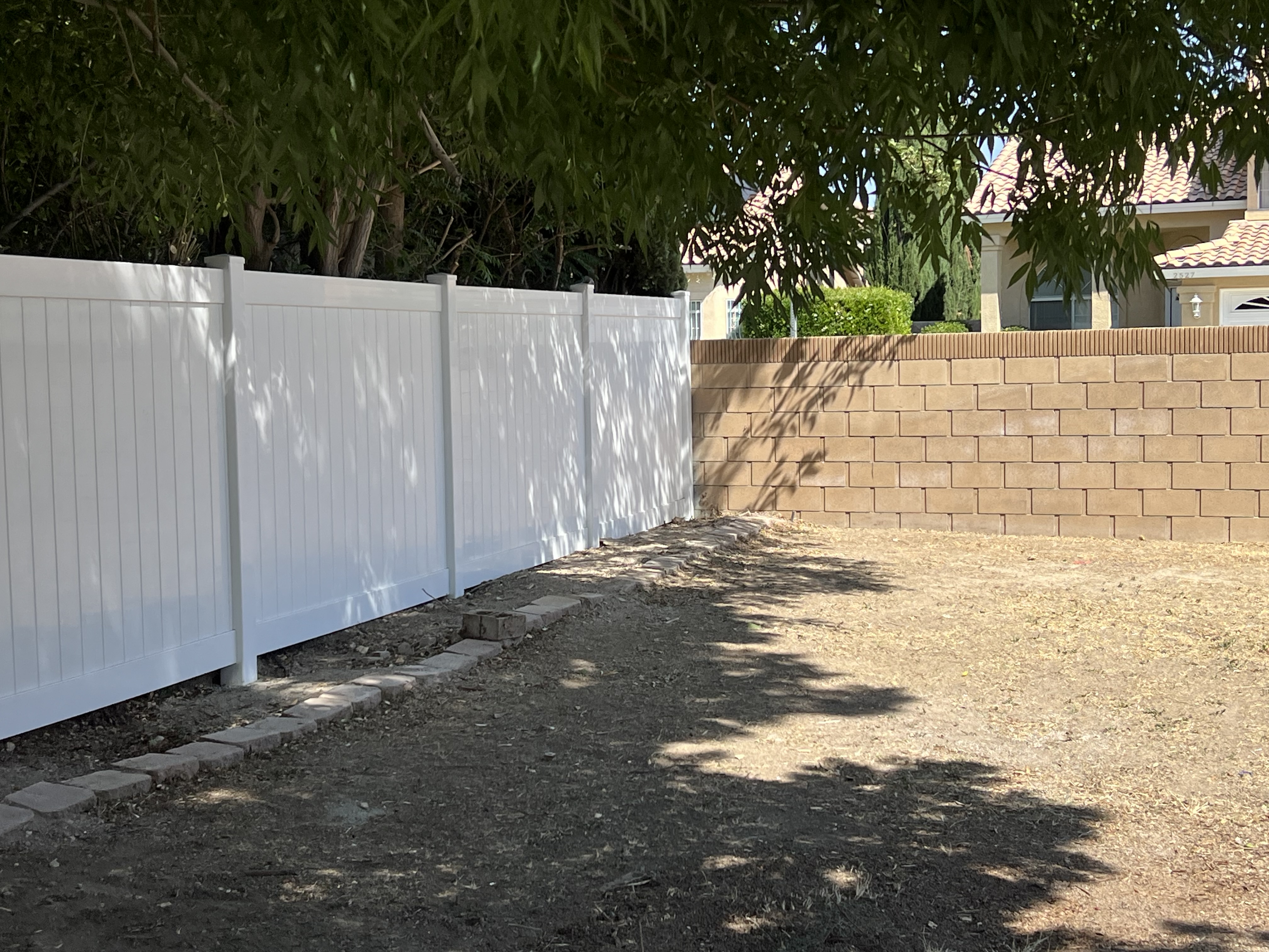 White vinyl privacy fence next to tan block wall — residential side yard